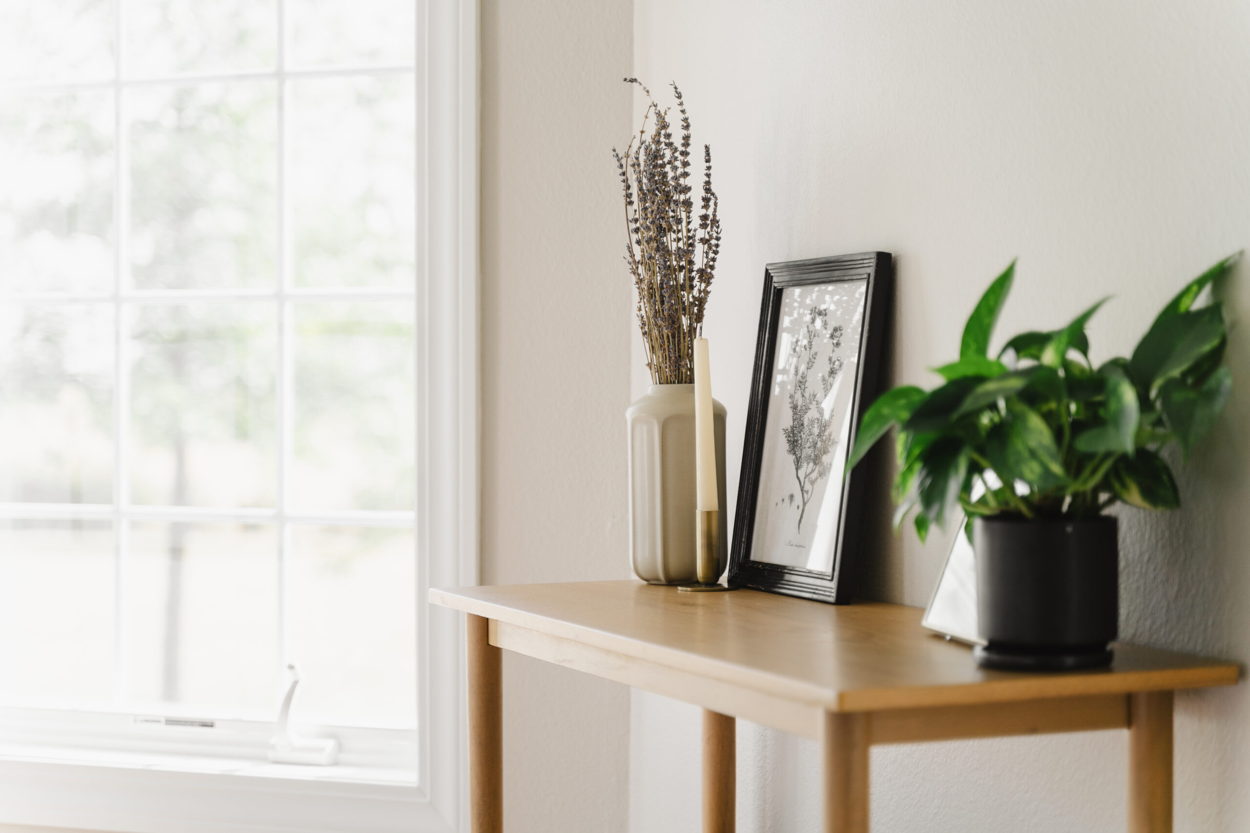 Wooden occasional table topped with plants and art next to window